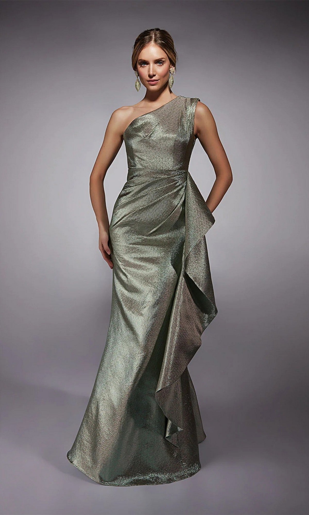 A woman in the Alyce 27751 long formal dress, featuring a celadon metallic jacquard one-shoulder design with side ruffle detail, stands against a plain gray background.